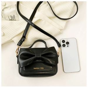 Détail d'un mini sac noir avec un grand nœud décoratif et des finitions dorées
