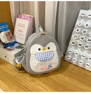 Detail of penguin backpack featuring transparent pocket with colorful pom-poms and charm