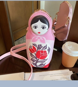 Detailed view of pink Russian doll crossbody bag on a table showing unique doll face design