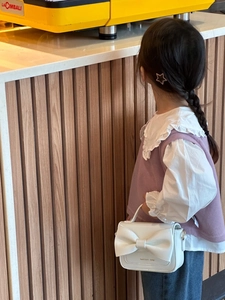 Détail d'un mini sac à main blanc avec un grand nœud porté par un enfant au café
