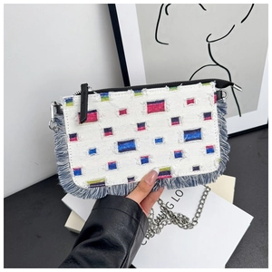 Detail of white denim crossbody bag featuring colorful fringe patches and silver chain