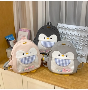 Detail view of penguin backpacks with colorful pom-poms and matching charms in 3 colors