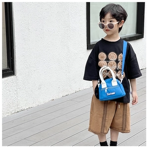 Outdoor shot of a blue mini kids crossbody bag with white handles and letter logo