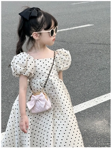 Détail d'un sac bandoulière rose matelassé avec nœud porté sur une robe à pois de fille