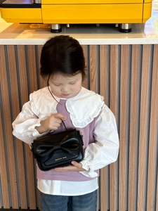 Détail d'une fille tenant un sac à main noir en cuir avec un grand nœud décoratif