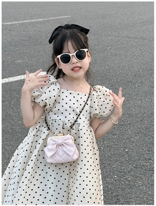 Fille en robe blanche à pois avec mini sac matelassé rose et accessoires de nœud
