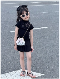 Détail d'une jupe plissée noire pour fille avec un petit sac à bandoulière matelassé