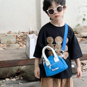Blue kids crossbody bag with white handles shown in an outdoor park setting