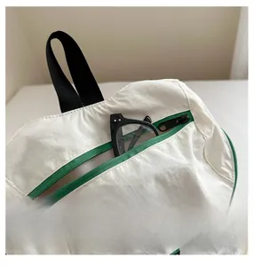 Détail du sac à dos blanc en nylon avec poche avant, fermeture éclair verte et sangle noire
