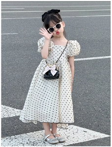 Détail d'un sac bandoulière matelassé noir avec nœud sur une robe à pois pour petite fille