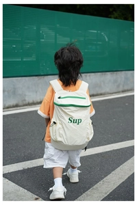 Sac à dos enfant blanc cassé avec zip vert et lettrage Sup dans un décor de rue