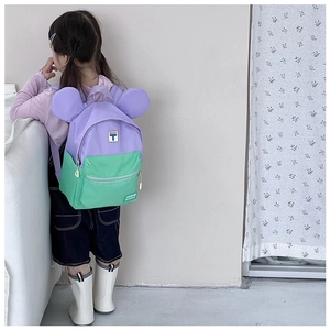 Side view of cute purple and green schoolbag with big ears on a young girl model
