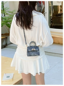 Détail d'un mini sac bandoulière bleu texture denim avec boucle argentée sur robe blanche