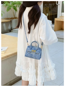 Sac bandoulière mini en denim avec boucles dorées porté sur une robe blanche en extérieur