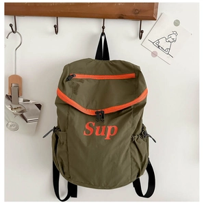 Détail du sac à dos enfant vert avec zip orange et texte sur crochet mural en bois
