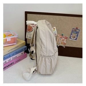 Vue latérale du sac à dos scolaire en toile beige avec poches latérales élastiques