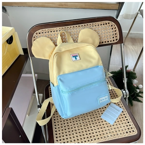 Detail of yellow and blue kids backpack with round ears on a vintage rattan chair