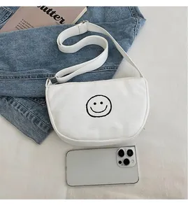 Close-up of white canvas crescent bag with smiley face and size comparison with phone