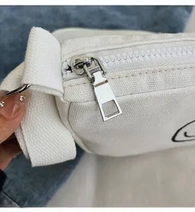 Detail of a smooth silver metal zipper on a white canvas shoulder bag for kids