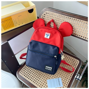 Detail of red and blue contrast kids backpack with cute round ears on a rattan chair
