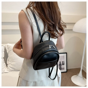 Mini black synthetic leather backpack shown on a model in a cozy home setting