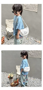 Close-up of white canvas kid's crossbody bag with smiling face and letter print