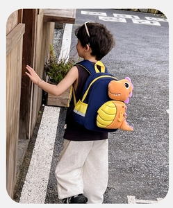 Dettaglio dello zaino dinosauro blu navy con peluche, strisce riflettenti e spallacci gialli