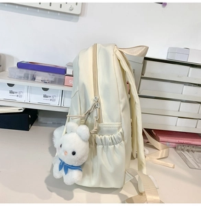 Side view of cream backpack featuring elastic pocket and a cute white bunny plush charm