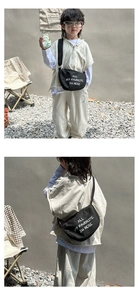 Detail of a kids' black canvas crossbody bag paired with a gray hooded leisure outfit