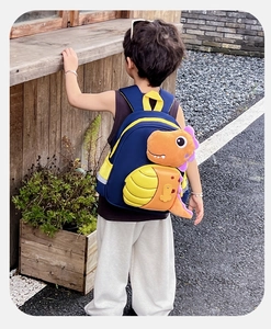 Dettaglio del dinosauro di peluche 3D sullo zaino blu per bambini con tasche a rete laterali