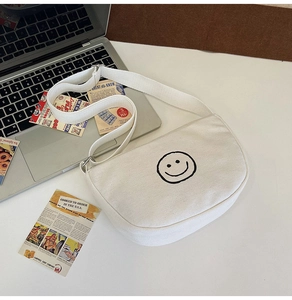 Close-up of white canvas crossbody bag with black smiley face print and adjustable strap