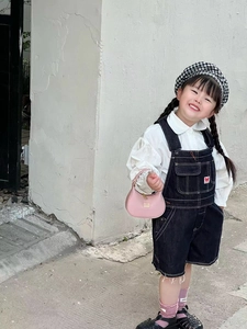 Detail of a pink luxury style leather handbag paired with denim overalls for children