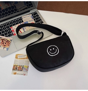 Close-up of black canvas crossbody bag with white smiley face print on white desk