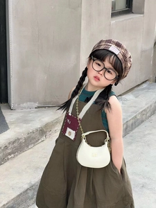 Detail view of stylish kids outfit featuring a brown pinafore dress and white mini bag