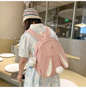 Pink rabbit backpack featuring 3D bunny ears and a plush doll charm in a lifestyle setting