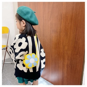 Toddler girl wearing a bright yellow flower crossbody bag with blue petals in a warm room