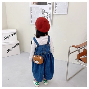 Detail of a kids bunny crossbody bag paired with denim overalls and a red beret