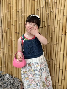 Detail of pink semi-circle handbag with chain and patterned dress on child model