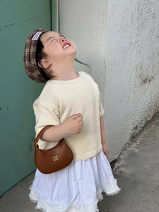 Close-up of a child wearing a brown crescent handbag and a plaid beret in a stylish outfit
