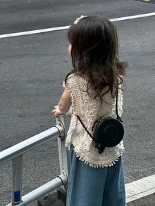 Detail of a child wearing a black round crossbody bag with a white crochet fringed vest