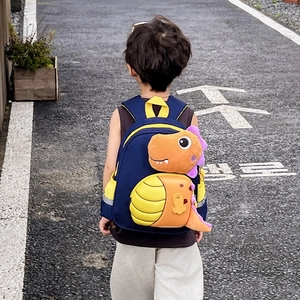 Zaino bimbi dinosauro blu scuro con peluche arancione su un sentiero all'aperto