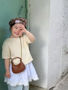 Close-up of children's brown saddle bag with gold chain strap on small fashion model