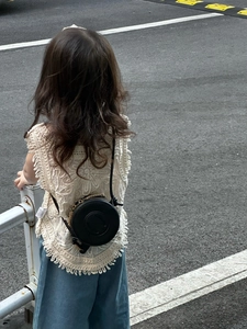 Detail view of a black round leather crossbody bag on a child outfit with crochet top