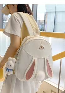 Detail of white rabbit ear backpack with plush charm and brand label on front pocket