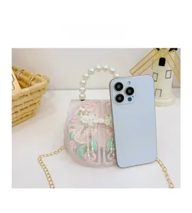 Detail of mini Chinese embroidery bag showing pearl handle and size comparison to phone