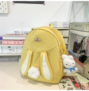 Detail of yellow rabbit ears backpack with plush bunny keychain on a cozy desk