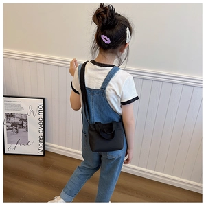 Rear view of a child wearing a minimalist black nylon crossbody bag with dual handles