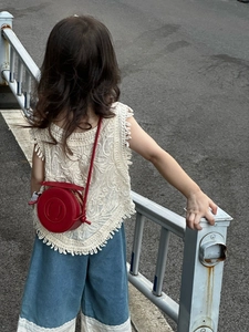Detail of a red round PU leather crossbody bag paired with a white crochet tassel vest