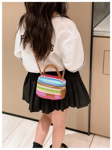 Detail of child wearing a colorful woven crossbody bag with chain strap and leather handle