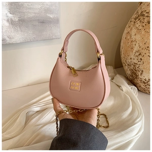 Close-up of a pink semi-circle mini bag with a gold chain strap on white fabric